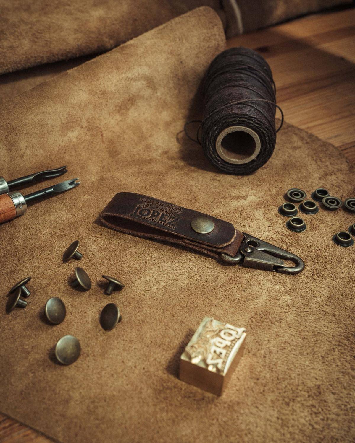 Suede hides, waxed thread, solid brass rivets and hardware, and edge tools laid out on the workbench